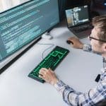 A professional working in front of a monitor with code, indicating he could be working to minimize ransomware risk.